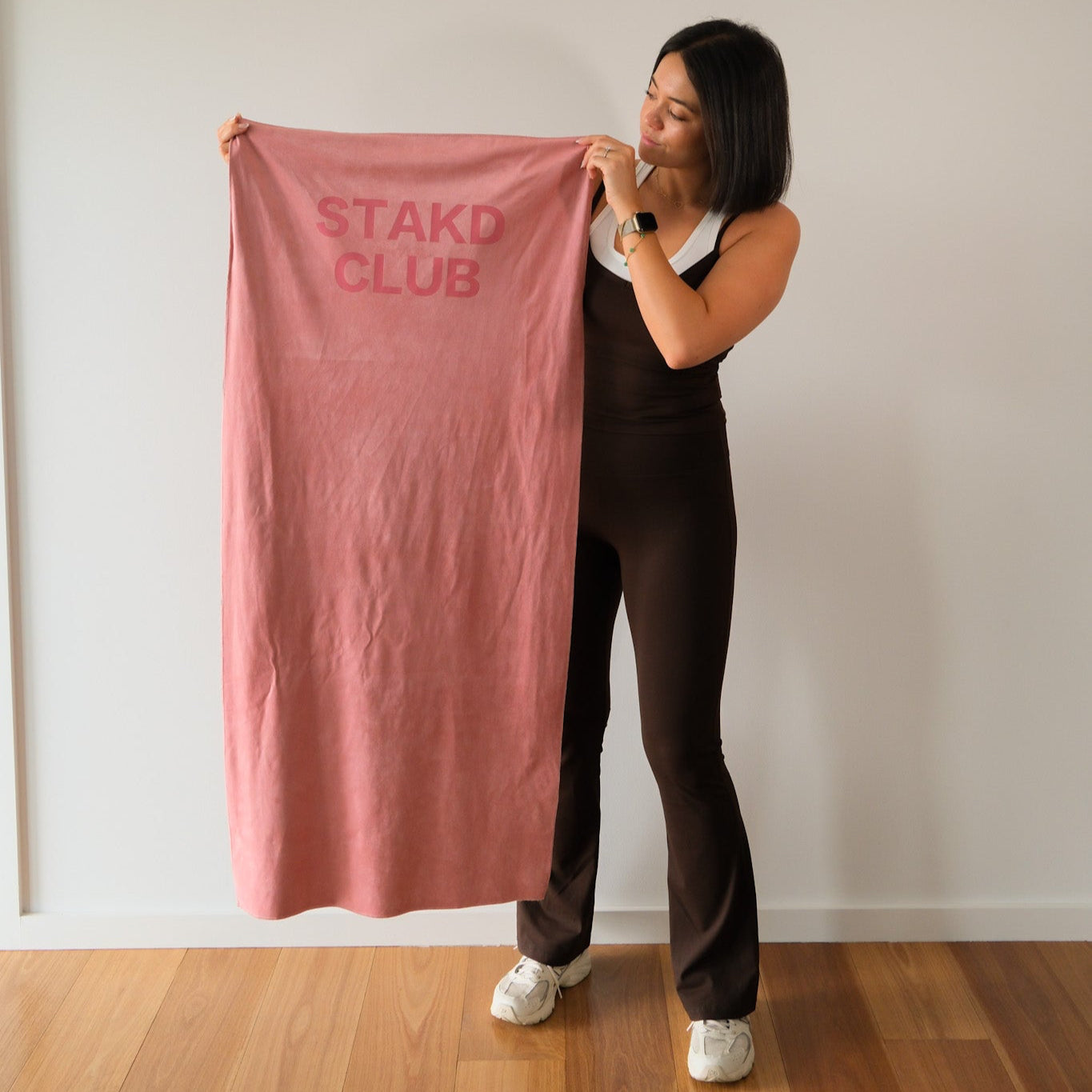 Person holding a pink towel with 'STAKD CLUB' text against a plain wall.