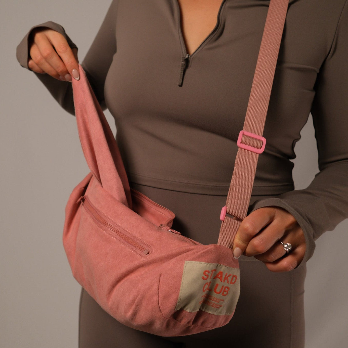 Person holding a pink sling bag with visible branding against a neutral background