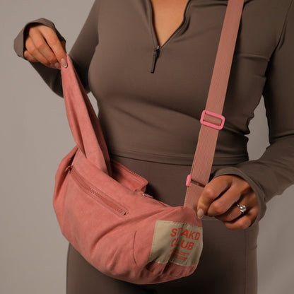 Person holding a pink sling bag with visible branding against a neutral background